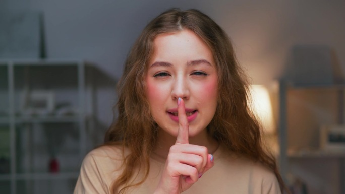 年轻女子看着相机的肖像，表现出紧闭嘴巴和闭上嘴巴的迹象。危险谈话中女性手势停止说话的面部特征。手势由