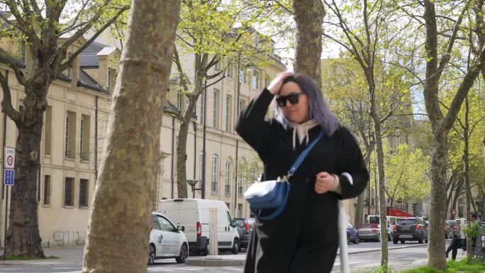 穿着大衣的时尚年轻女子在阳光明媚的春日走在巴黎老街上。春天，戴着墨镜的时尚女性走在巴黎街头