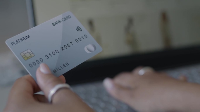 女性手持银行卡，在室内用笔记本电脑支付网上购物的特写