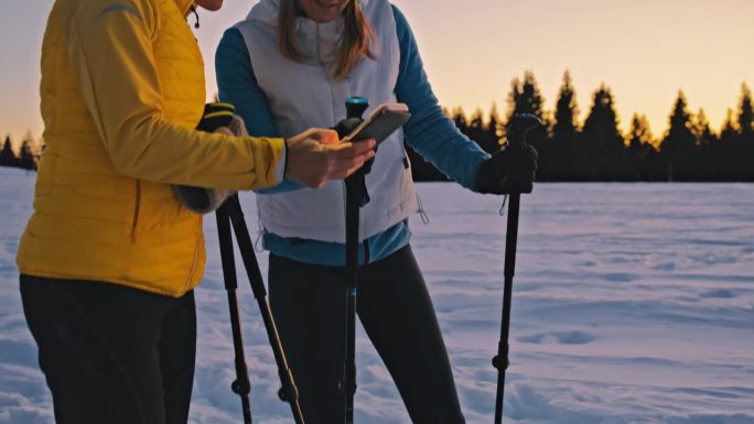 两个女人在冬天的乡村雪地里走雪鞋时正在看手机