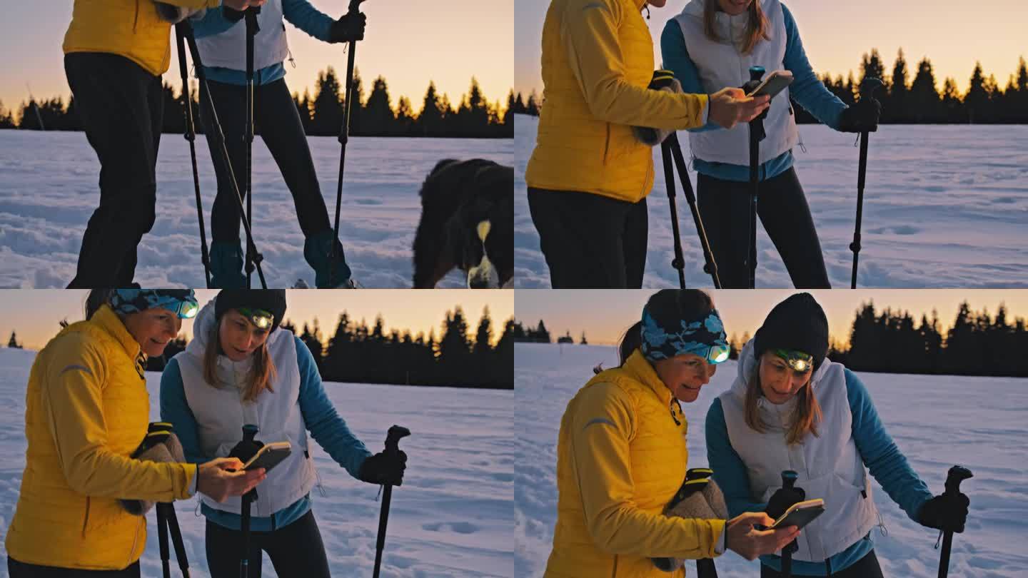 两个女人在冬天的乡村雪地里走雪鞋时正在看手机
