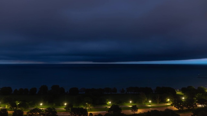 一团乌云在密歇根湖上空翻滚，暴风雨的时间流逝，天气锋面覆盖了夜晚的天空，交通信号灯在前景中划过湖岸大