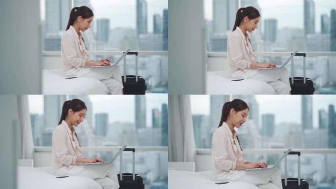 亚洲女商人用科技笔记本电脑在床上工作，而在市中心带着行李箱进入房间或办公室