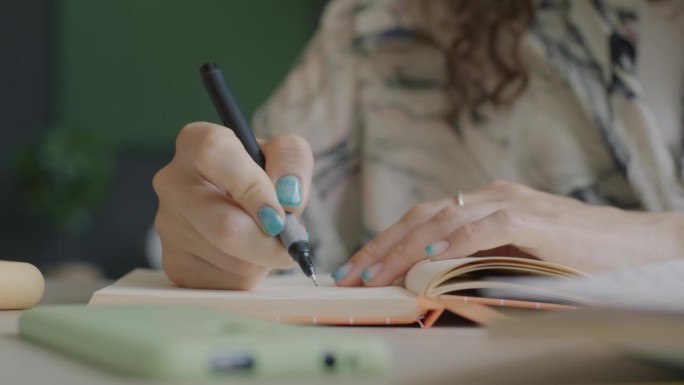 女性手拿着笔在桌上的笔记本上写笔记的特写