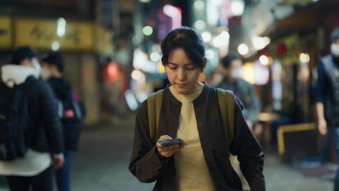 亚洲女子在美丽的夜城中漫步，她给朋友发短信讲述她的旅行