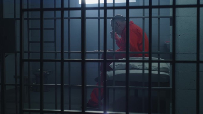 身穿橙色制服的老年囚犯坐在牢房里吃东西