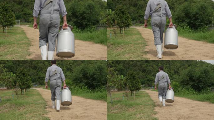 一个男奶农拿着一个大牛奶罐走在农场外面