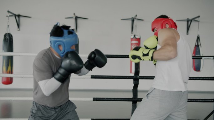 年轻男子拳击手戴着头盔和手套在健身房一起训练出拳的慢动作