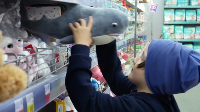 一个可爱的男孩在玩具店拿着一个玩具鲨鱼并仔细检查它