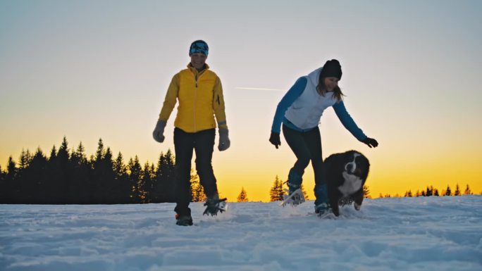 日落时分，两个女人在雪山上遛狗