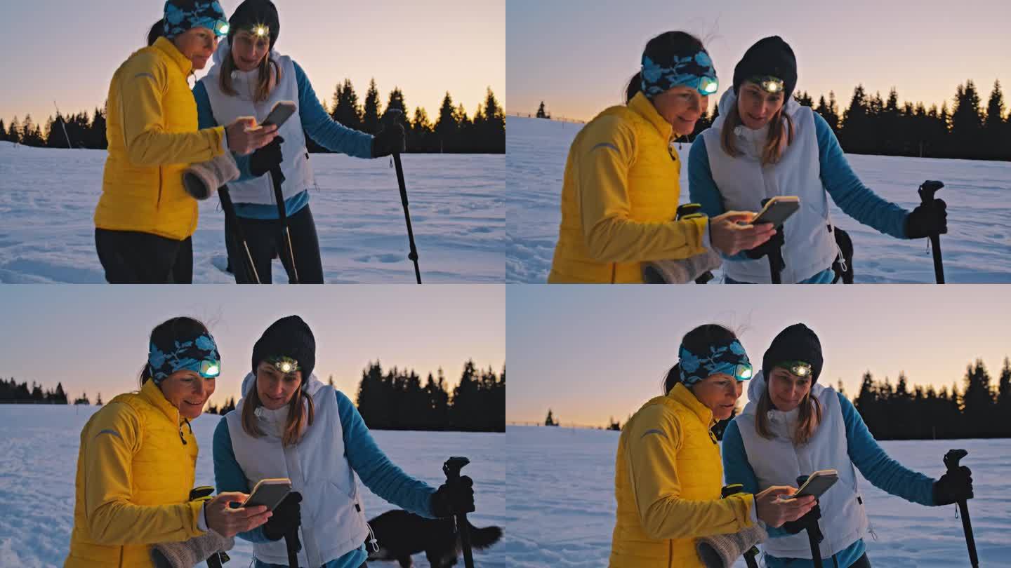 两个女人和她们的狗在冬天的乡下雪地里走雪鞋时正在看手机