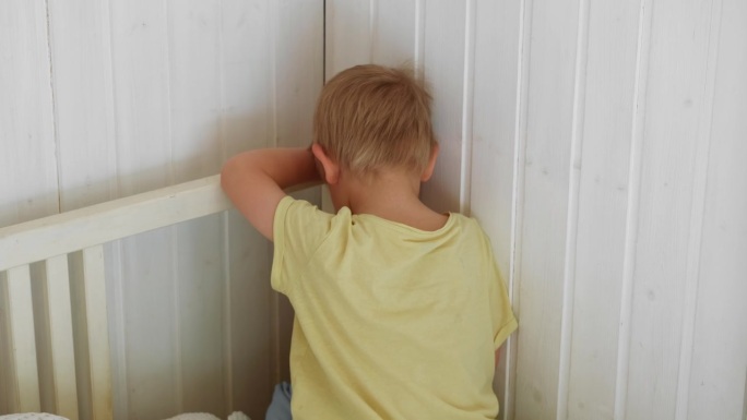 孩子受到惩罚。蹒跚学步的男孩在角落里靠墙坐着，因为他淘气，做了不好的负面行为。沮丧、体贴的小孩。在家