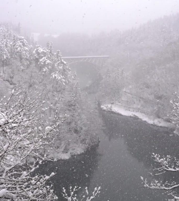 4K无人机鸟瞰图，雪天横跨河上的山之间的铁路桥。