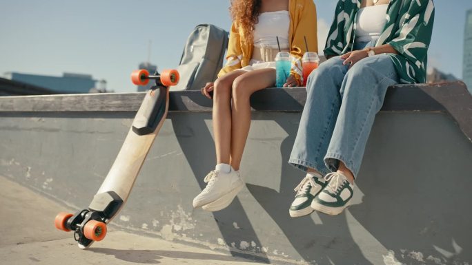 女友们，滑板鞋，在滑板公园和一群人坐在一起，在城墙边喝酒。夏天，户外和z世代女性一起在城市空间里喝着