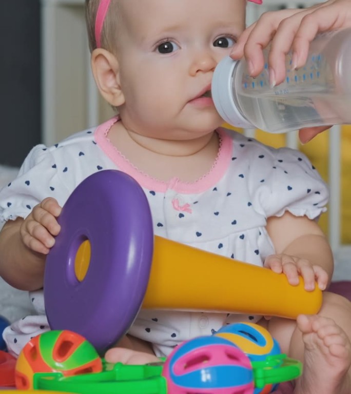女婴边玩边从瓶子里喝水