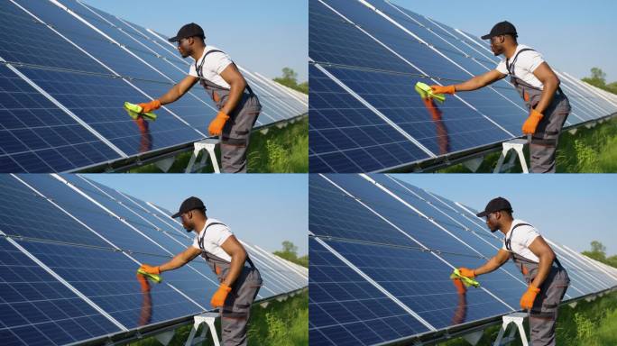 替代发电厂的工人穿着制服用拖把清洁太阳能电池板。英俊的非裔美国人在照顾设备。