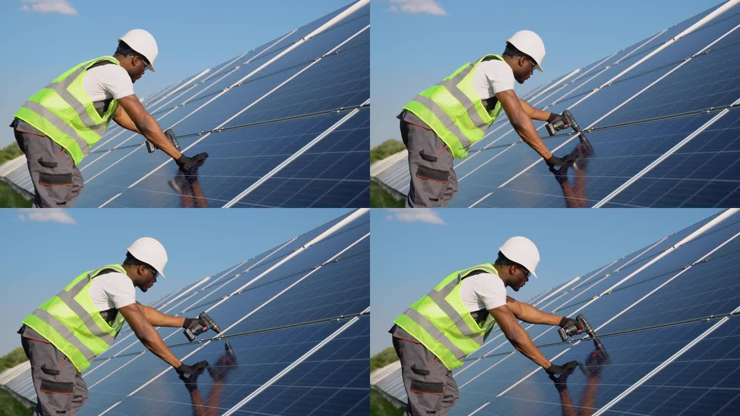 戴着白色头盔的年轻英俊的非裔美国机械师用电钻在太阳能电池板上打洞