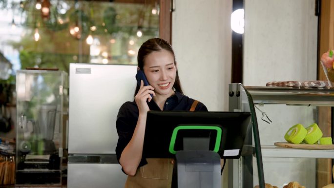 一个拥有小生意的亚洲美女。开咖啡店接受电话订餐的顾客的订单准备咖啡。站在咖啡厅柜台后面准备饮料。