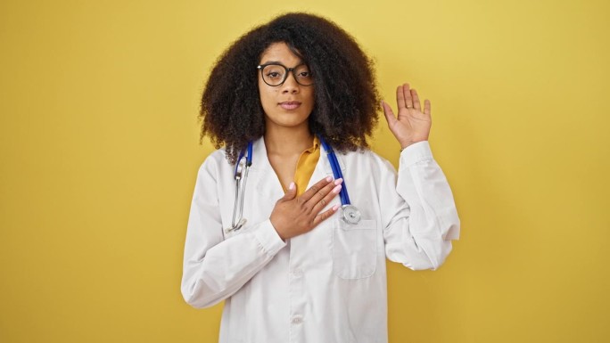 非裔美国女医生在孤立的黄色背景上把手放在胸前宣誓