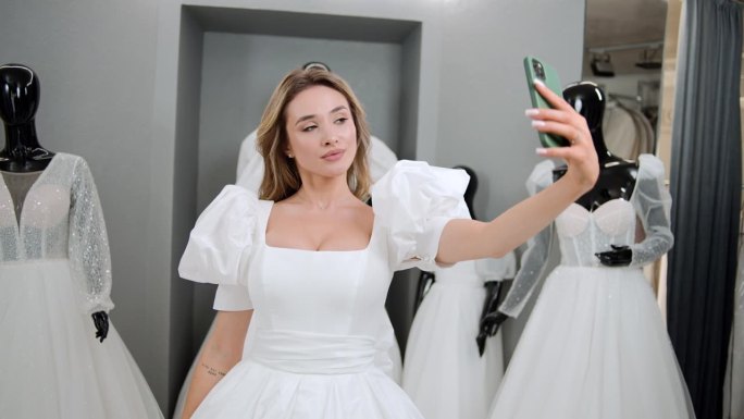 金发新娘在婚礼沙龙试婚纱时用智能手机自拍的照片