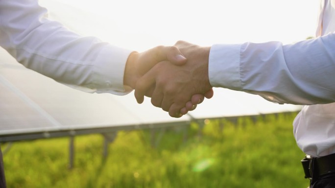 两位工程师、投资者或商人在讨论完光伏太阳能板的背景后握手