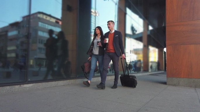 年轻的商务夫妇带着一个手提箱走在市中心去酒店的路上，在出差时寻找房间