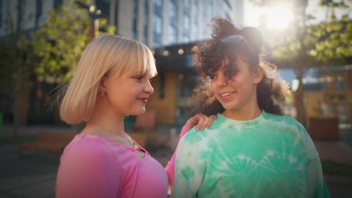 两个时髦的少女在城市街道上看着镜头微笑。在阳光明媚的夏日，年轻时尚的女性在市中心放松。青年文化观。