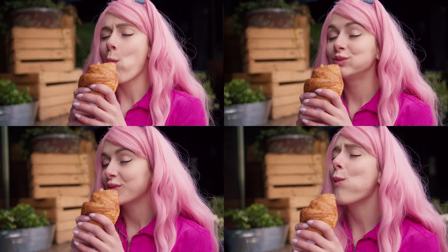 一个粉色头发的女孩真的很喜欢毛茸茸的羊角面包。边走边吃零食