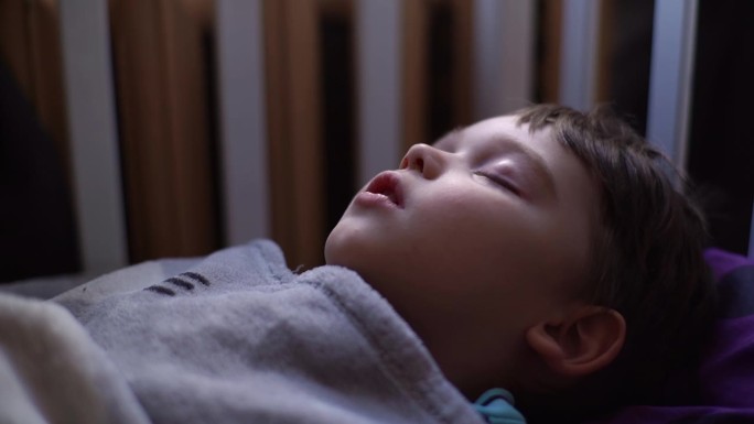 3岁小孩的特写侧视图，小男孩张着嘴睡觉，深呼吸，在床上的毯子下躺着做梦