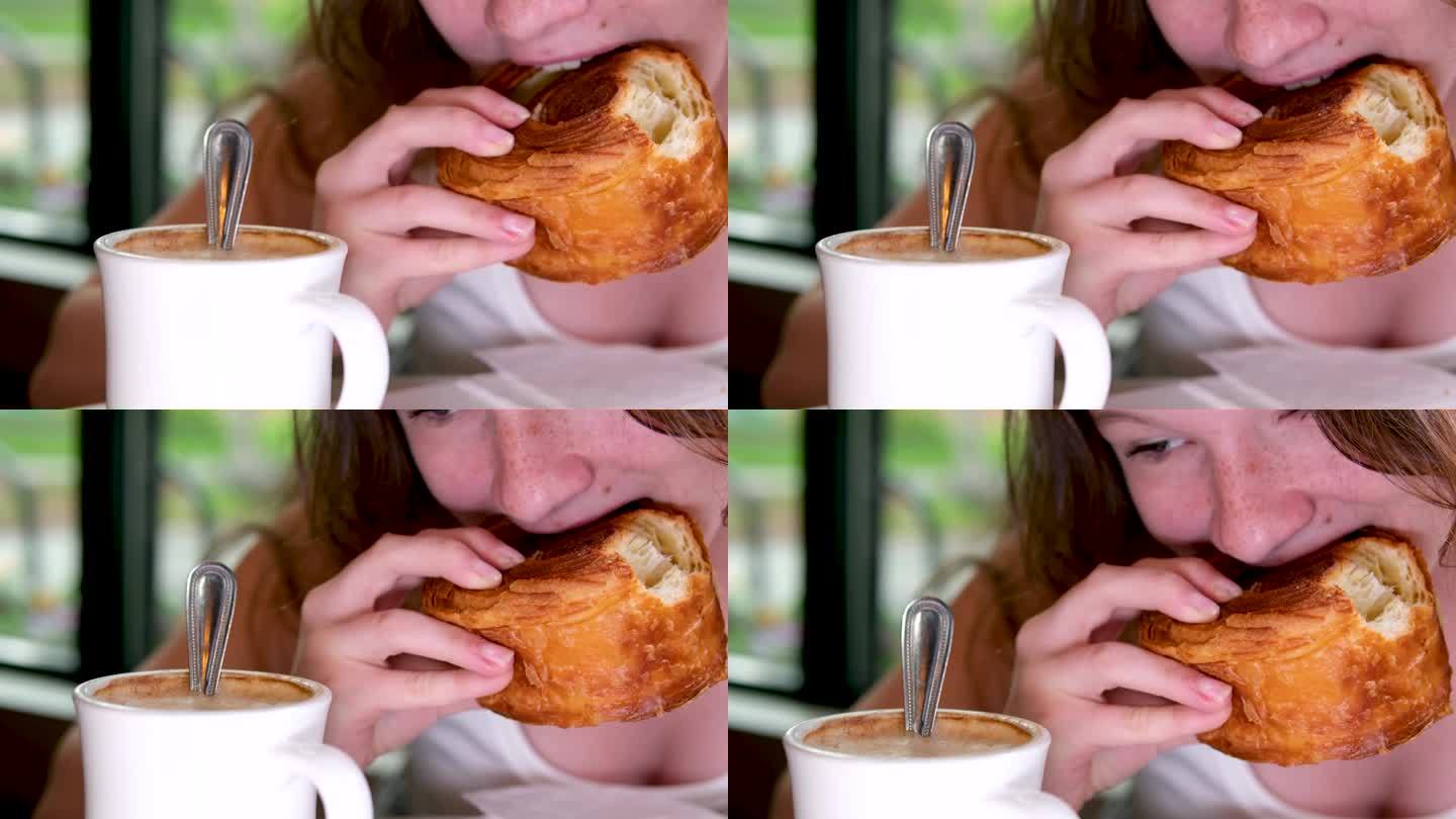 女人撕下一块美味的新鲜羊角面包，手的特写镜头。女士在咖啡馆吃点心，阳光从旁边洒下来