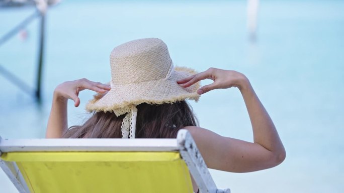 慢动作女人坐在沙滩椅上，戴着遮阳帽