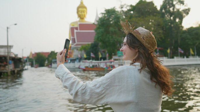 曼谷，一名女子坐在河边，以金佛为背景自拍