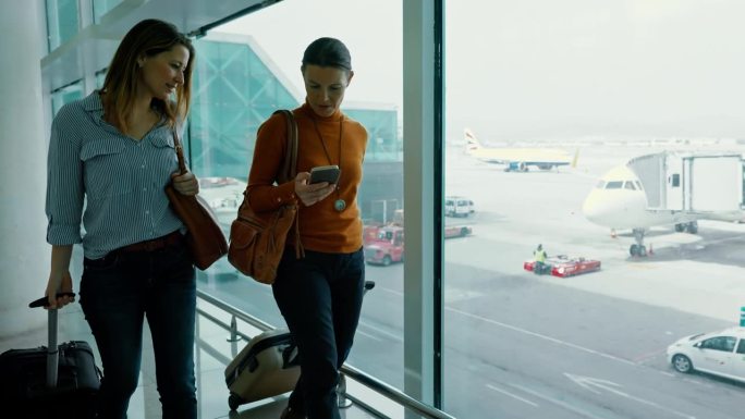 两名女性在机场门口行走时使用智能手机