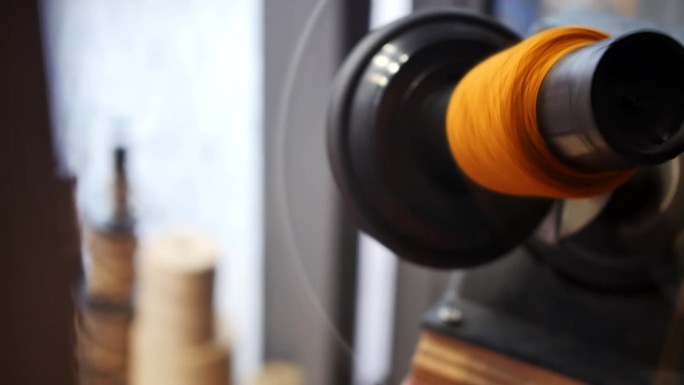 橙色纱线在旋转的羊毛绕线机上绕线的特写。纺织和羊毛工业。羊毛制线
