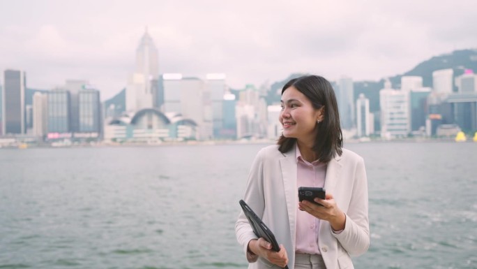 走在香港商业中心中心的女商人用你的手机来协调工作。