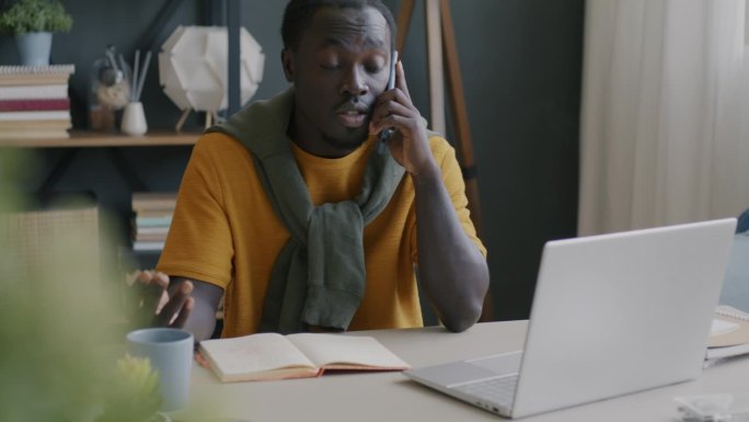 自由职业者非裔美国人在家里用手机看笔记本电脑屏幕