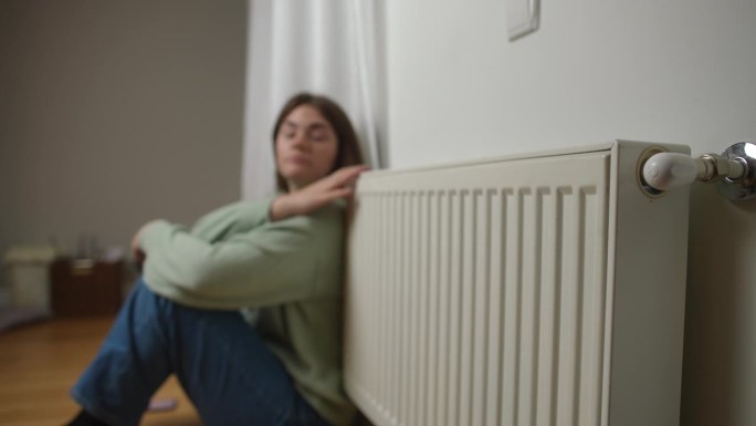 家用暖气片，背景是年轻女子坐在地板上揉着胳膊说话。侧视图无法辨认的白人女士在家里做热身。