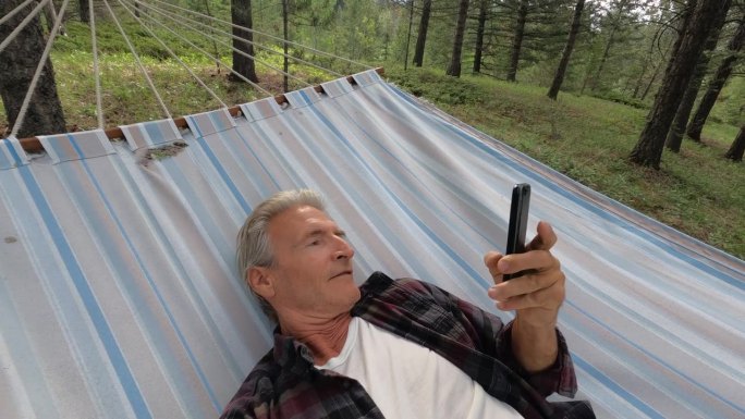 老人在吊床上休息，查看智能手机