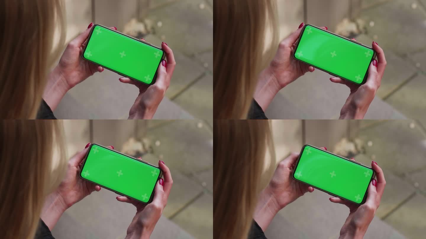 近距离双手女子手持使用白色手机横屏绿色屏幕坐在繁忙的街道上翻页冲浪上网技术智能手机短信手机
