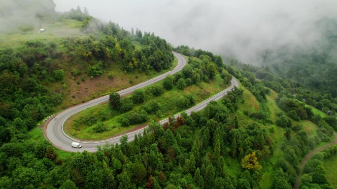 无人机航拍的山路蜿蜒穿过森林，穿过云层