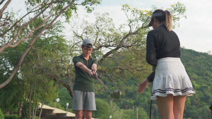 活跃的女高尔夫球手在高尔夫球场教一个男孩如何打高尔夫球