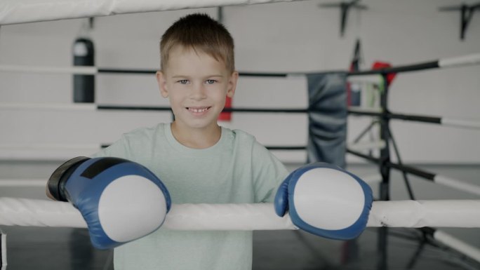 快乐的孩子的慢动作肖像年轻的拳击手戴着手套站在环微笑看着镜头