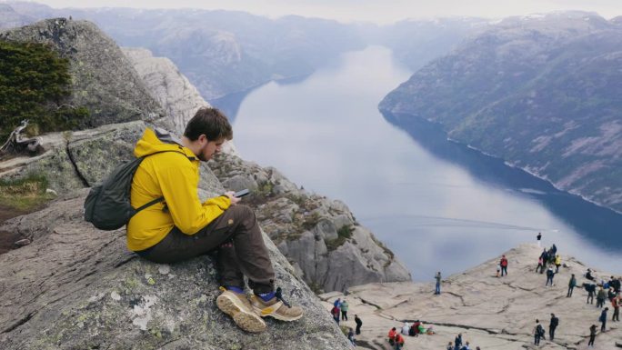 在挪威布道石山顶上使用智能手机的男子侧视图
