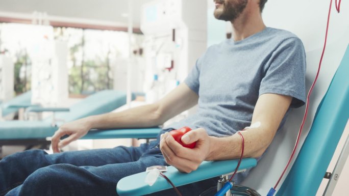 男性献血者的手的特写镜头。白人男子挤压心形红球，将血液通过管道泵入袋中。器官移植病人的捐赠。