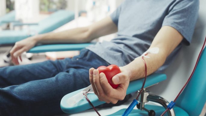 男性献血者的手的特写镜头。白人男子挤压心形红球，将血液通过管道泵入袋中。为烧伤病人捐款。