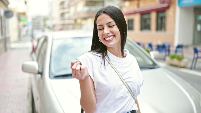 年轻漂亮的西班牙女人拿着钥匙站在路边的车旁