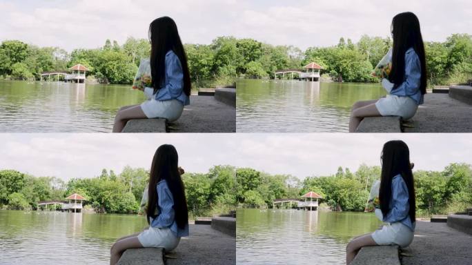 美丽的女孩坐在湖边晃着双腿。喂公园池塘里的鱼。购买彩色面包加入到你的饮食中。扔面包让鱼在大池子里游。