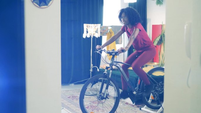 一位非洲妇女正在家里练习骑自行车。运动在家，健身在家的理念。