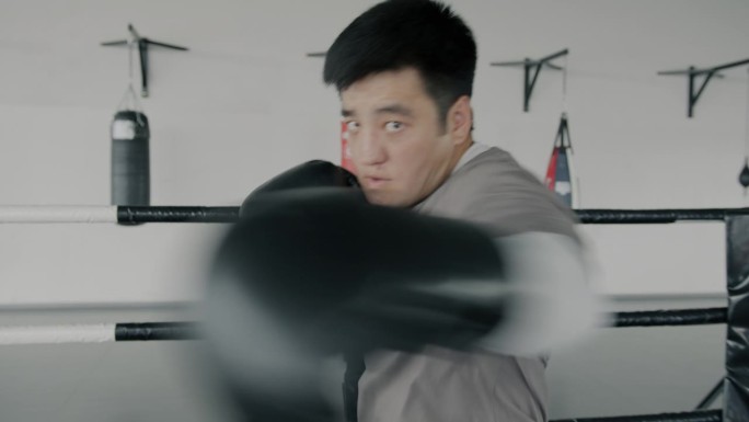 年轻的亚洲拳击手影子搏击，投掷拳头，看着摄像机在健身房的慢动作肖像