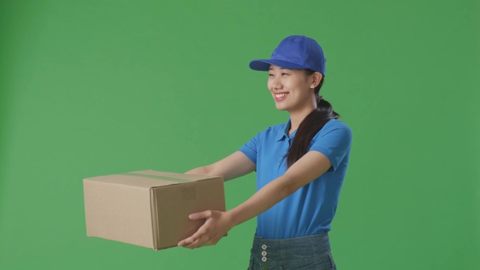 穿着蓝色制服的亚洲女快递员在工作室绿屏背景下微笑着给人送纸盒
